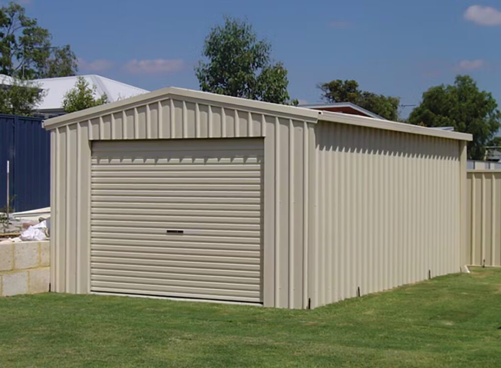 A beige metal garage with a closed roller door on a green lawn.
